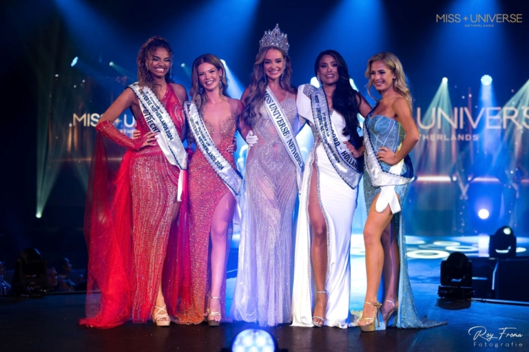 Five contestants in the Miss contest are on stage in their pretty dresses.